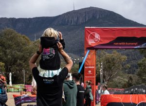 Image of child on adult's shoulders, near the start/finish line for Kunanyi mountain run, with the mountain in the background